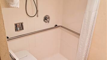 A bathroom with a shower, grab bars, a toilet, and a towel rack.
