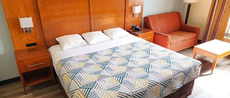 Una habitación de hotel con una cama grande, una mesita de noche, una silla y una pequeña mesa.