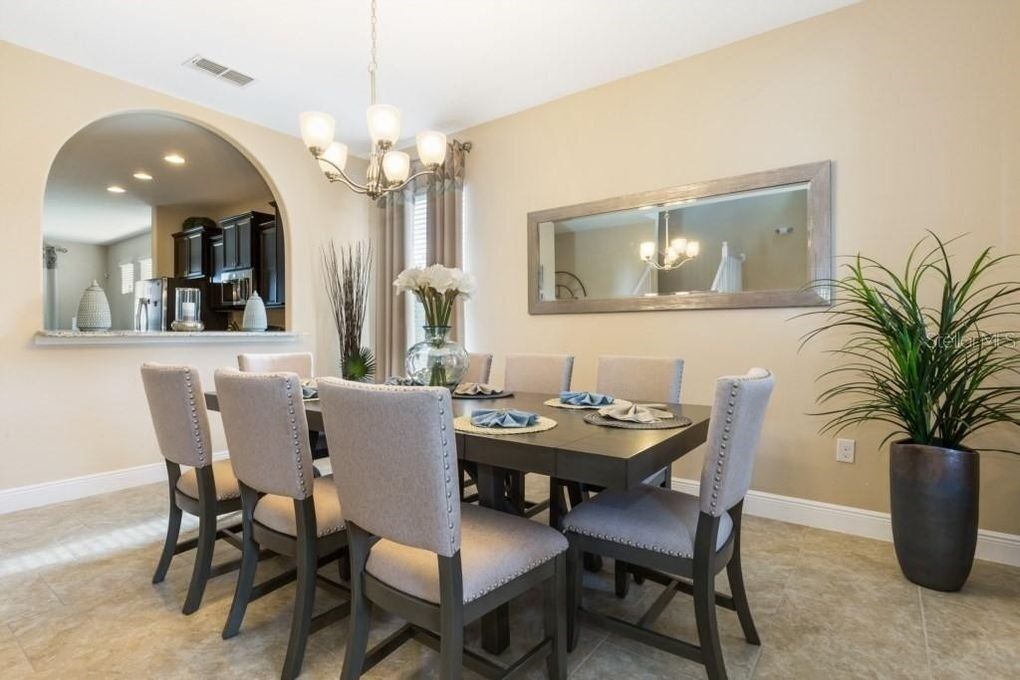 A dining area with a rectangular table, six chairs, a chandelier, a mirror, and a potted plant.