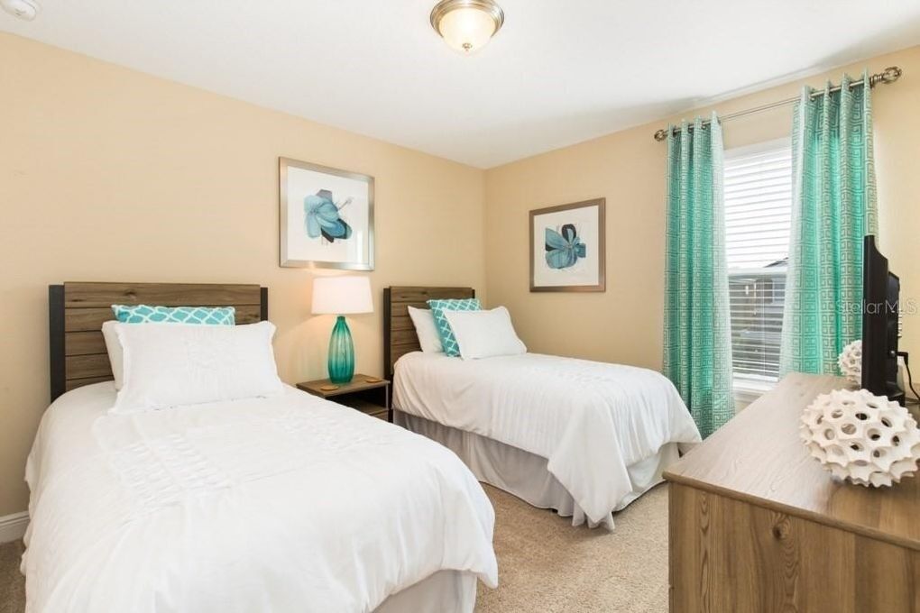 A hotel room with two beds, a wooden nightstand with a lamp, and a desk with decorative items.