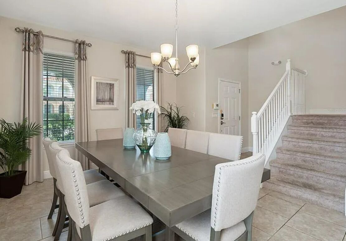 Een eethoek met een grote tafel, beklede witte stoelen, een kroonluchter en een trap.