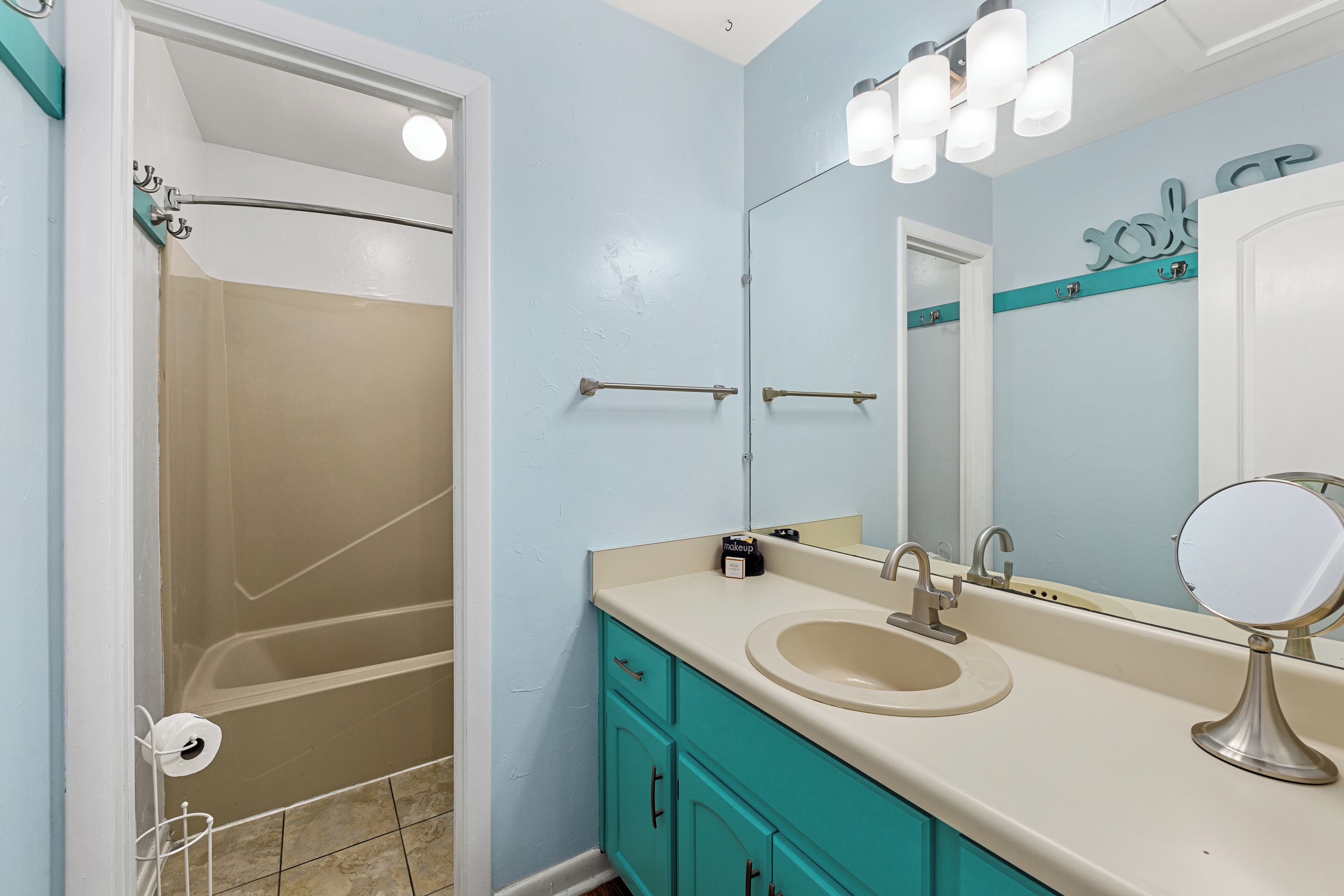 A bathroom with a bathtub, a sink, a vanity with cabinets, a mirror, and a towel rack.