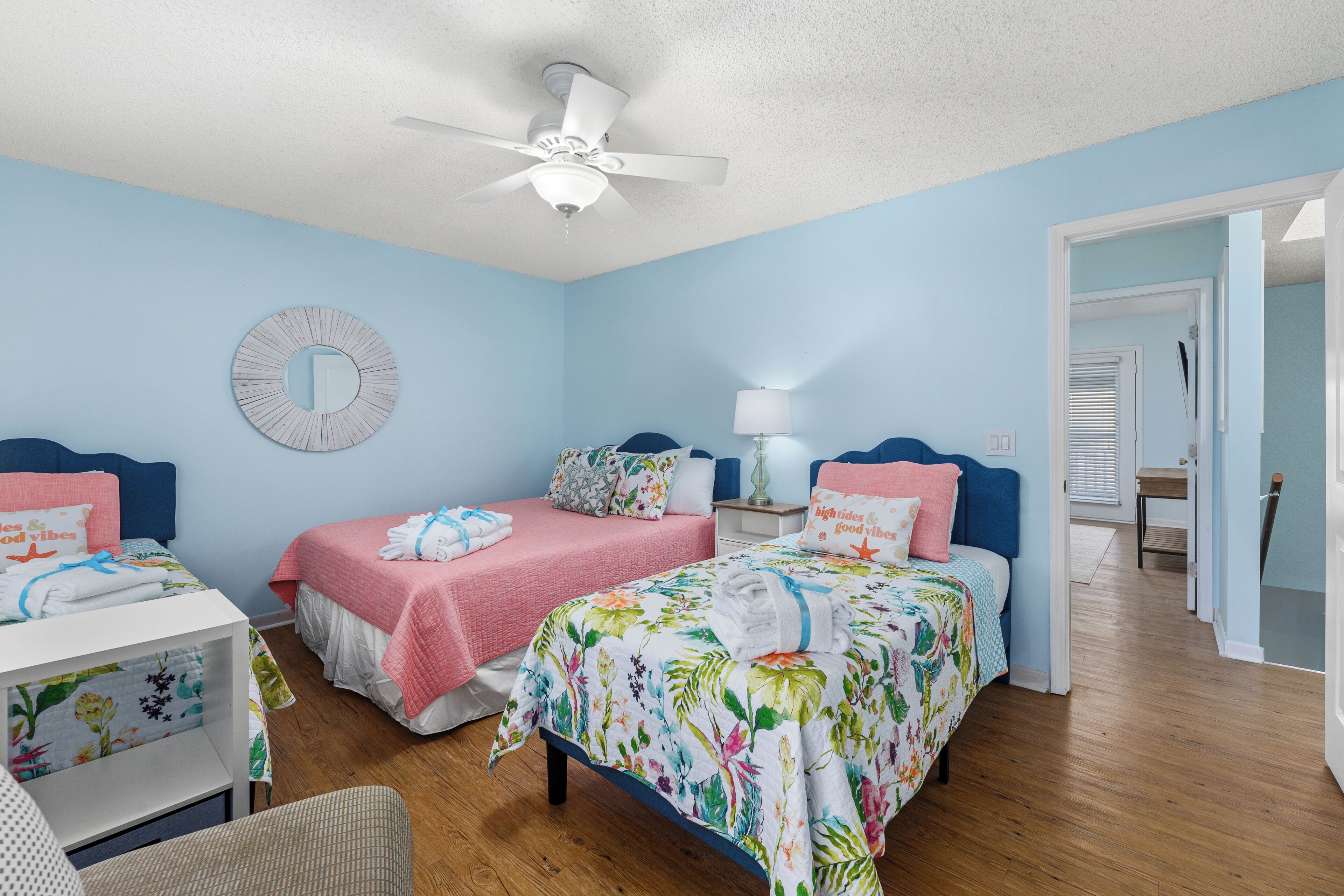 A bedroom with two beds, a ceiling fan, a round mirror, and a nightstand with a lamp.