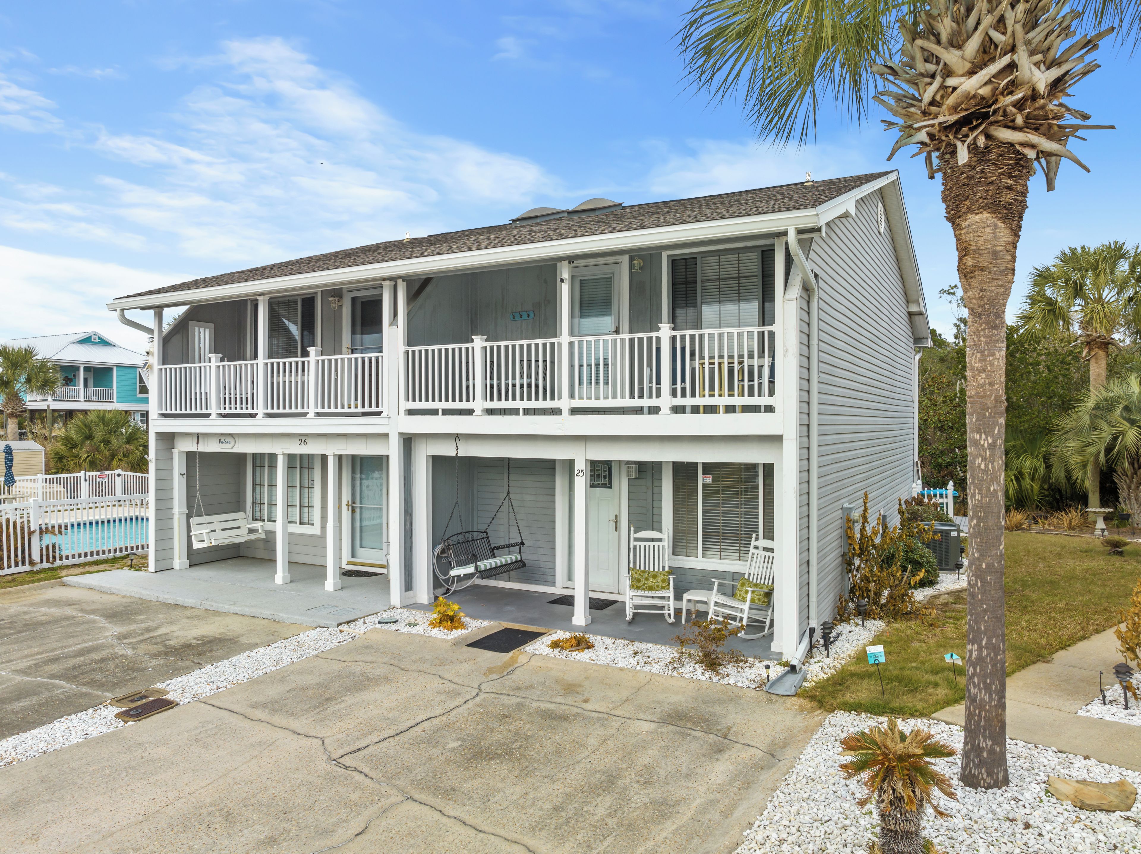 A two-story building with a balcony, a pool, and a palm tree.