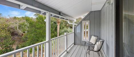 A covered porch with a white railing, a table with chairs, and a view of the surrounding greenery.