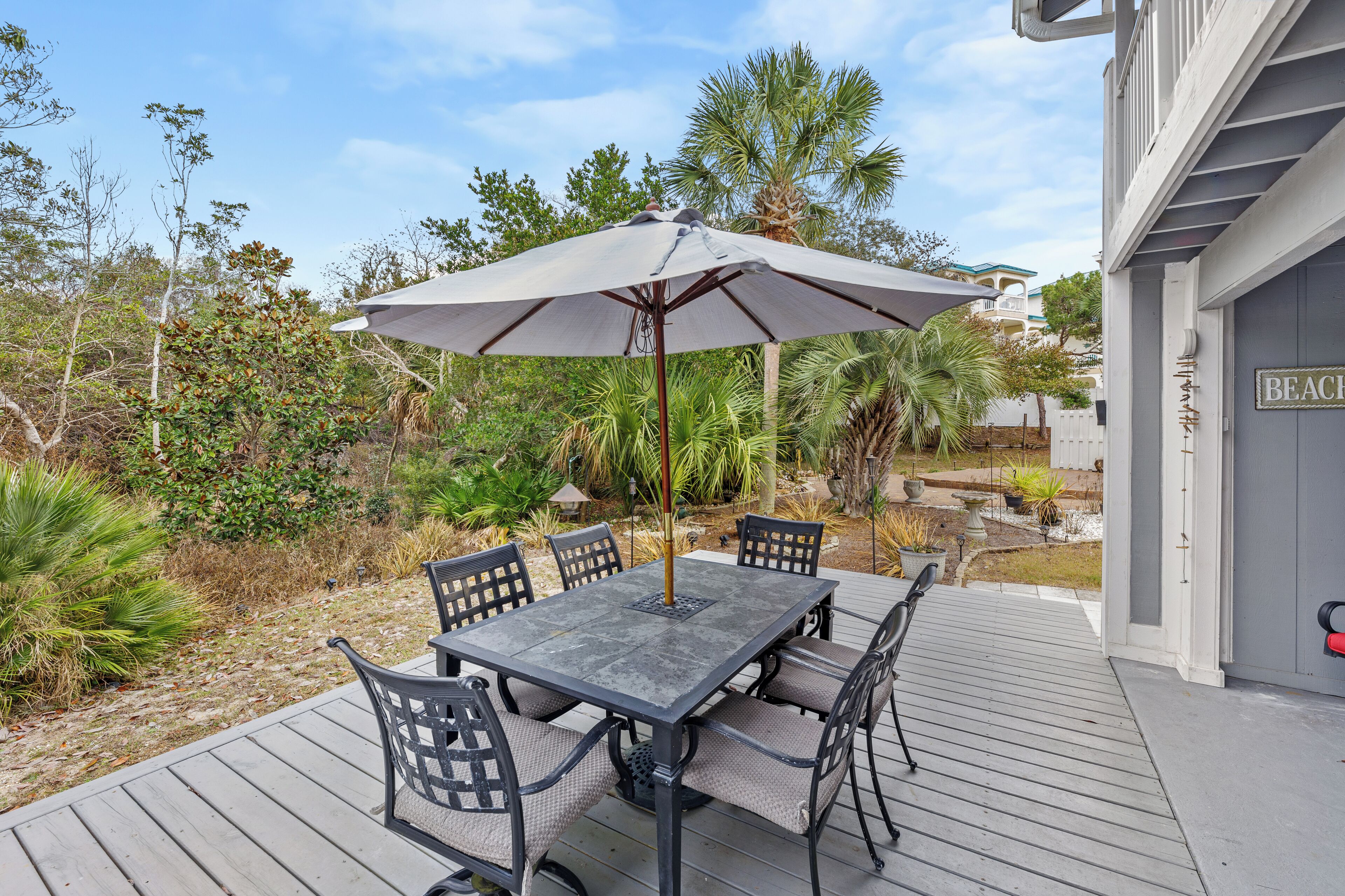 A patio with a table and chairs, surrounded by plants and a palm tree.