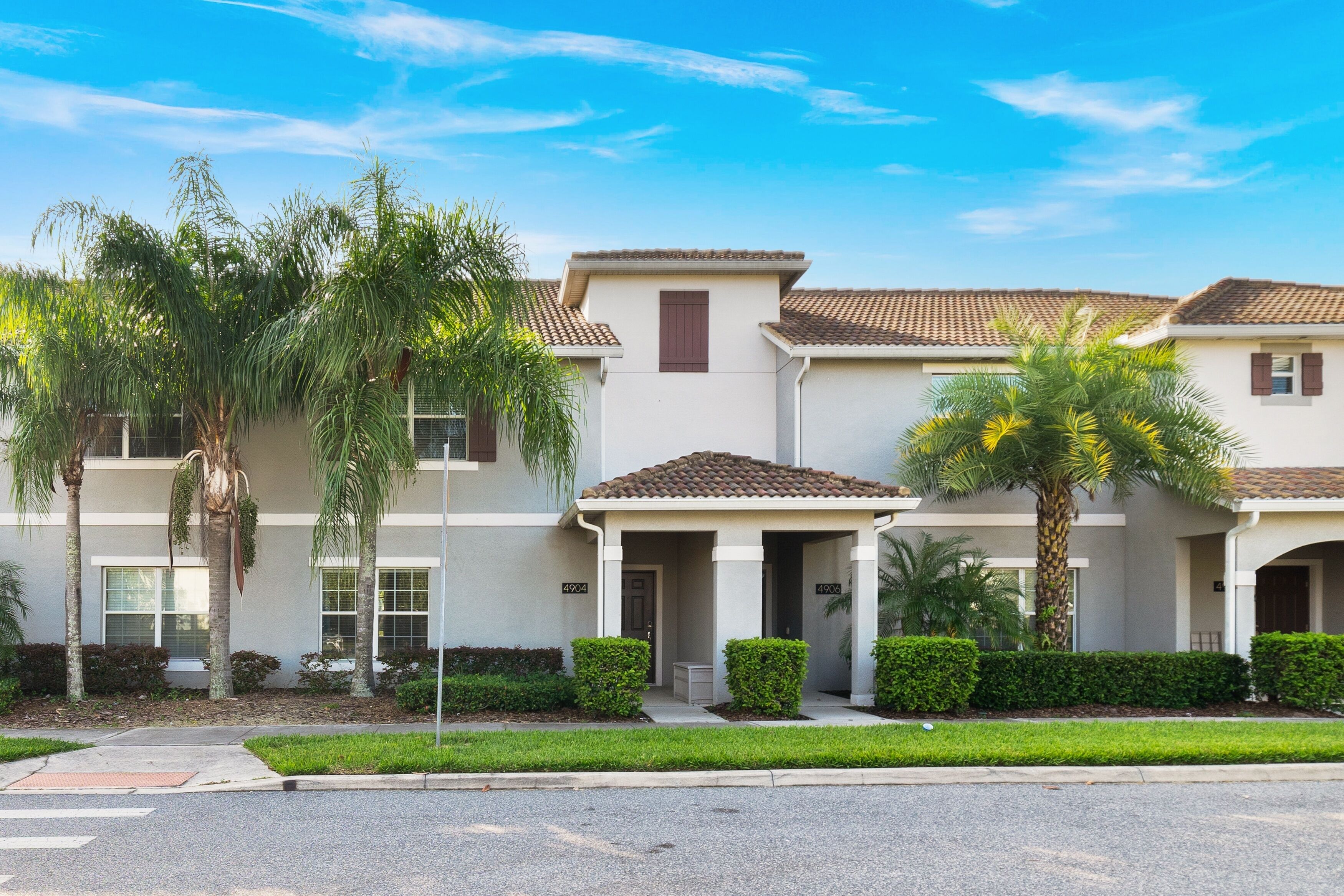 A row of townhouses with a covered front porch, palm trees, and a clear blue sky.