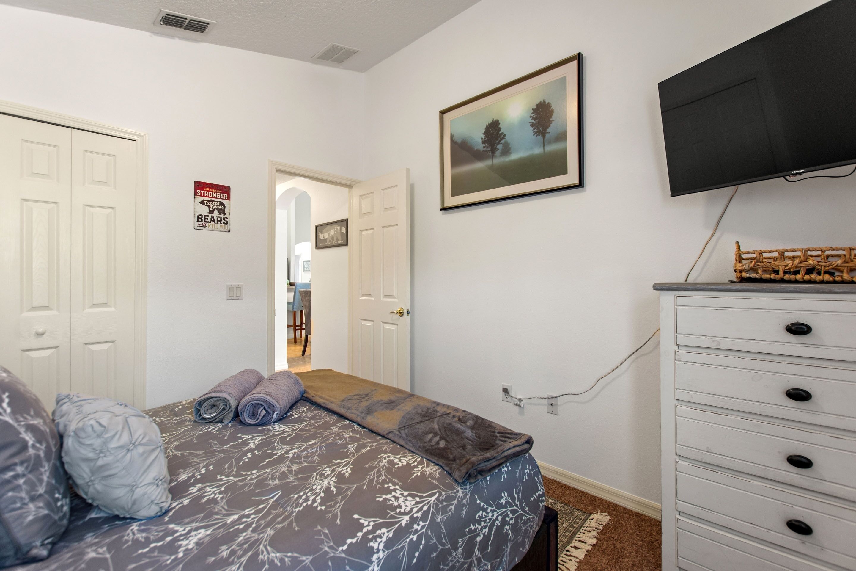 A bedroom with a bed, a dresser, a television, and a door leading to another room.