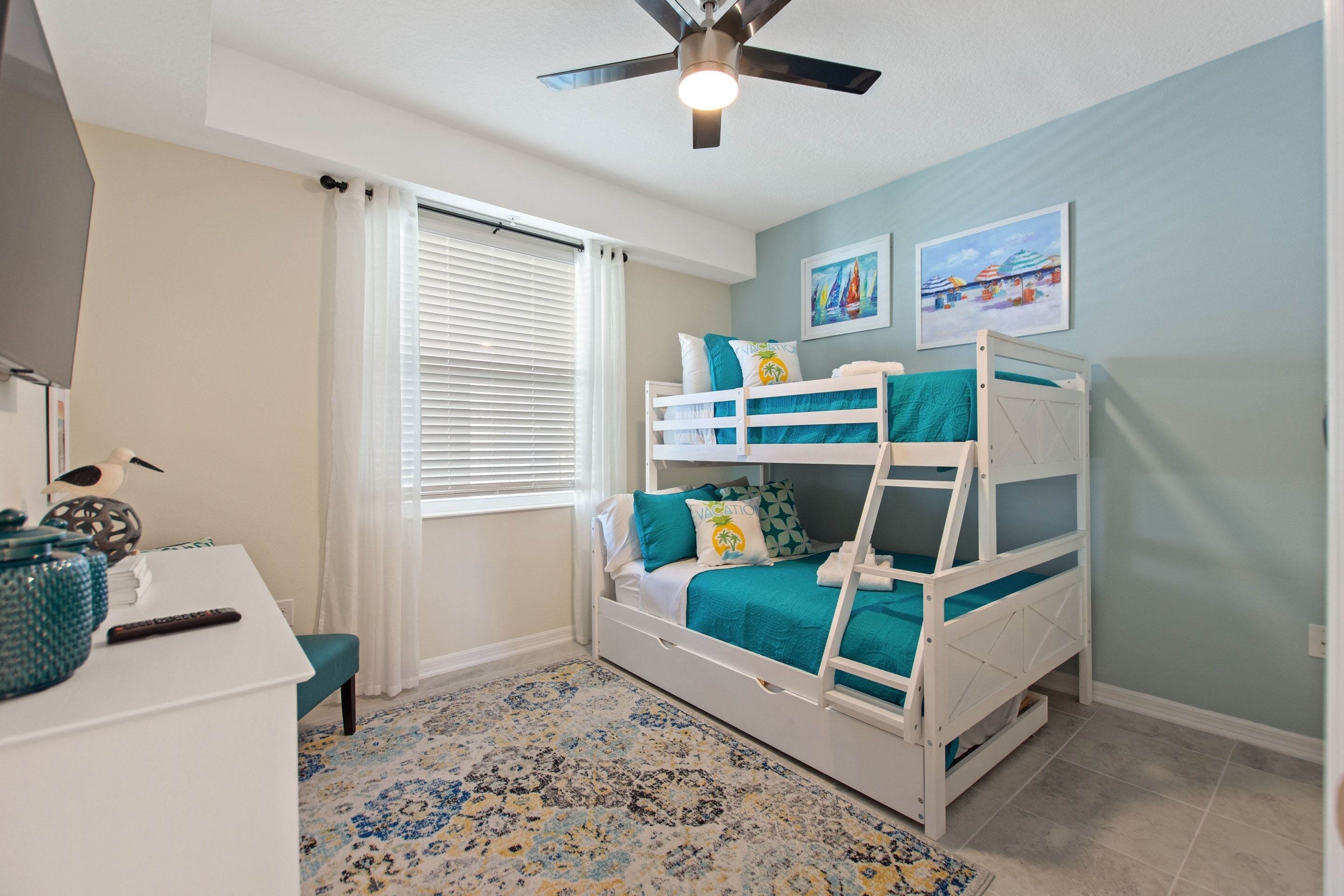 A child's bedroom with bunk beds, a desk, and a ceiling fan.