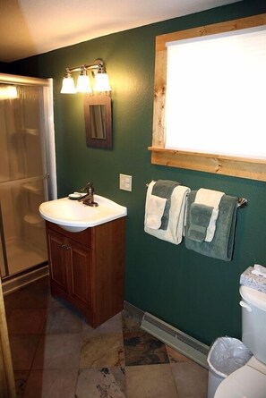 A bathroom with a white sink, wooden cabinets, a towel rack with two towels, a window above the sink, and a shower area. - Charming Cabin, Next To National Park 3 Bedroom Cabin - #20-NCD0297 (Estes Park)