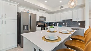 A modern kitchen with white cabinetry, stainless steel appliances, and a central island with seating. - Serenity Haven, Bliss, Storey Lake By Shine Villas 2 Bedroom Condo (Kissimmee)