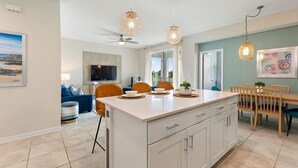 A modern kitchen with a central island, pendant lights, and a dining area with wooden chairs and a table. - Serenity Haven, Bliss, Storey Lake By Shine Villas 2 Bedroom Condo (Kissimmee)