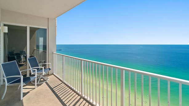 A balcony with two blue chairs, a glass door leading to an interior space, and a view of the ocean. - Tidewater Beach Luxury Penthouse With Resort Amenities and a View! (Panama City Beach)