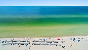 An aerial view of a beach with clear blue water, a sandy shore, and numerous beach umbrellas and chairs. - Tidewater Beach Luxury Penthouse With Resort Amenities and a View! (Panama City Beach)