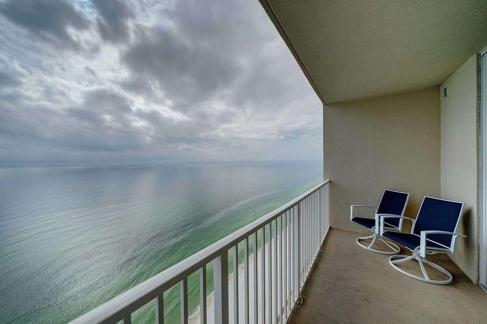 A balcony with a view of the ocean, two chairs, and a white railing.