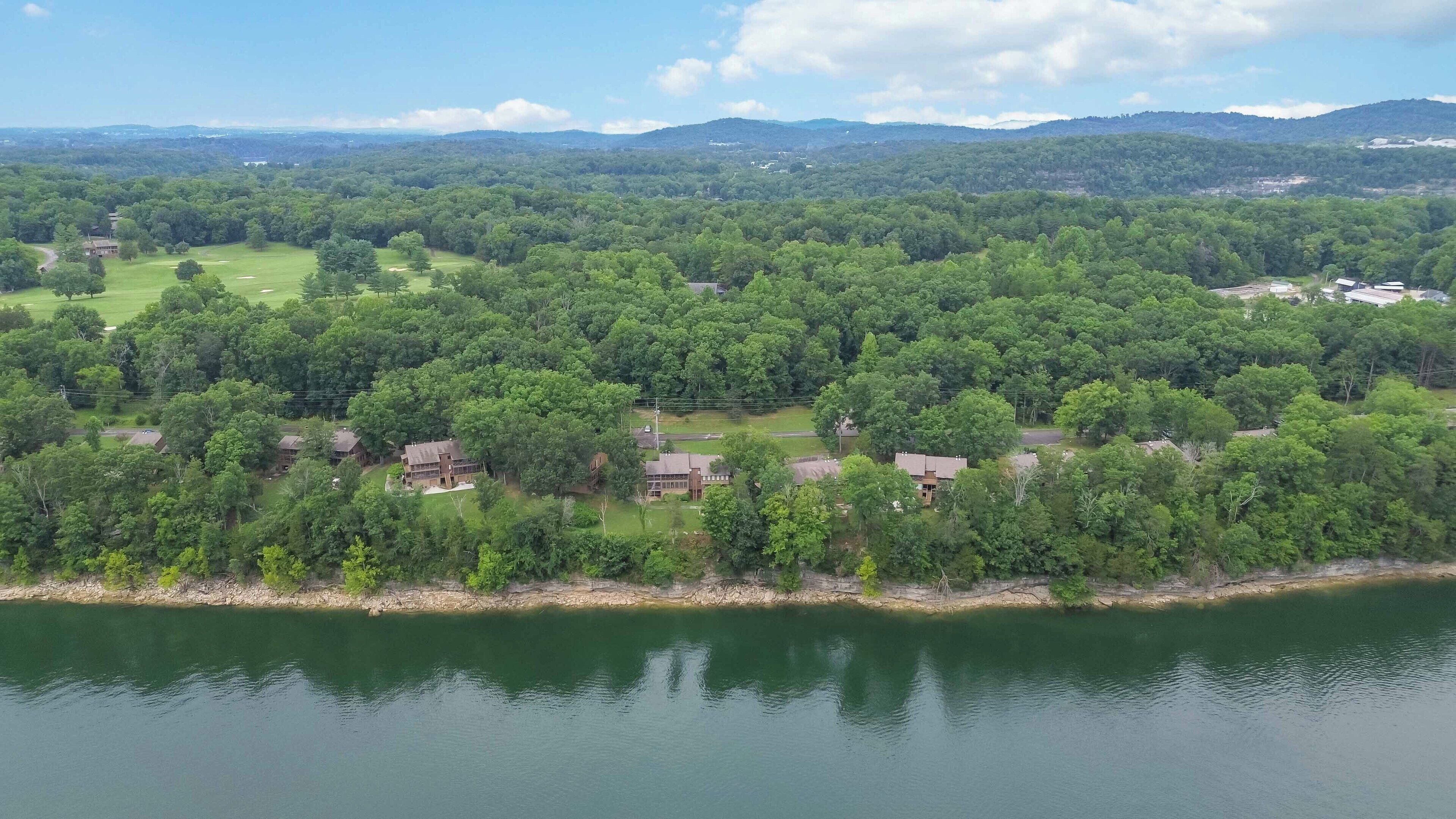A lakeside property with multiple buildings, surrounded by dense forest and hills in the background.