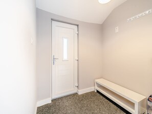 A hallway with a white door, a white bench, and a light switch on the wall.
