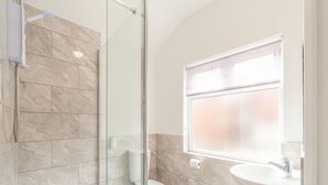 A bathroom with a glass shower enclosure, a toilet, and a sink with a window above it.