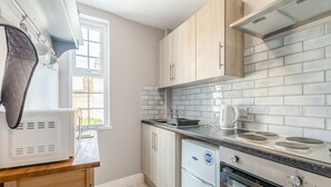 A kitchen with a window, a kettle, a toaster, a stove, and a refrigerator.
