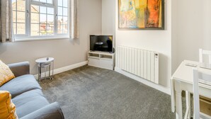 A living room with a sofa, a small table, a TV, a radiator, and a painting on the wall.
