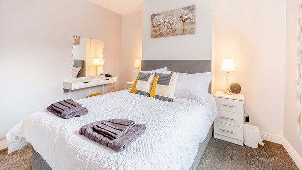 A neatly arranged bedroom with a bed, bedside tables, a mirror, and a wall-mounted artwork.