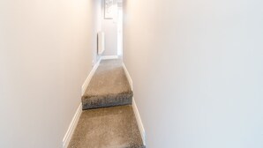 A narrow hallway with carpeted stairs leading to a door.