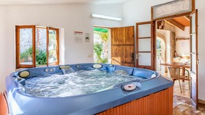 A hot tub in a room with wooden doors and a view of greenery outside.