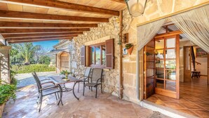 A covered patio area with stone walls, wooden beams, and a tiled floor.