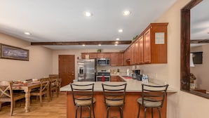 A kitchen with wooden cabinets, a stainless steel refrigerator, a microwave, and a dining area with a wooden table and chairs. - Smoky Mountain Abode - #CanPie Rancher# (Sevierville)