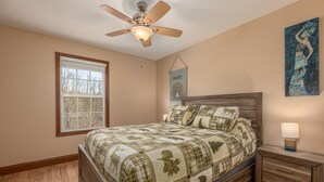 A bedroom with a wooden bed, a nightstand, a ceiling fan, a window, and a wall hanging. - Smoky Mountain Abode - #CanPie Rancher# (Sevierville)