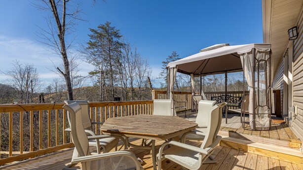 A wooden deck with outdoor furniture, a covered seating area, and a view of the surrounding landscape. - Smoky Mountain Abode - #CanPie Rancher# (Sevierville)