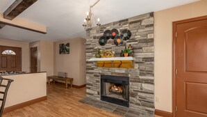 A living room with a stone fireplace, wooden flooring, a bench, and a door. - Smoky Mountain Abode - #CanPie Rancher# (Sevierville)