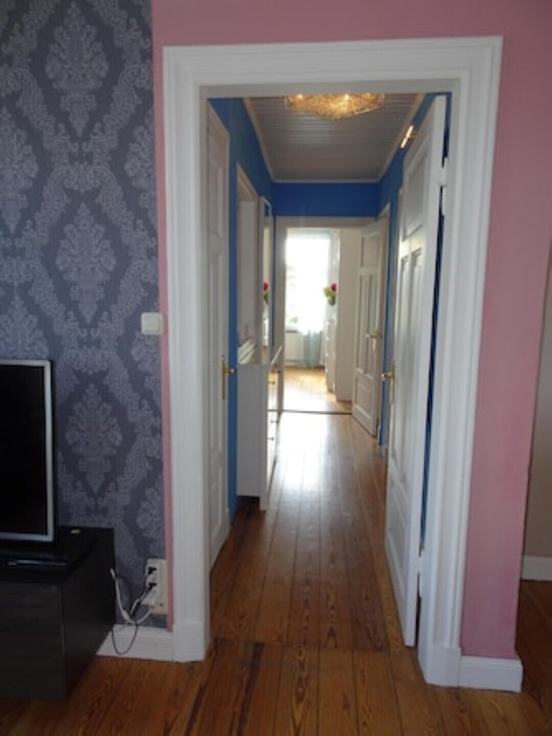 A hallway with wooden flooring, white doors, and a patterned wallpaper on one side.