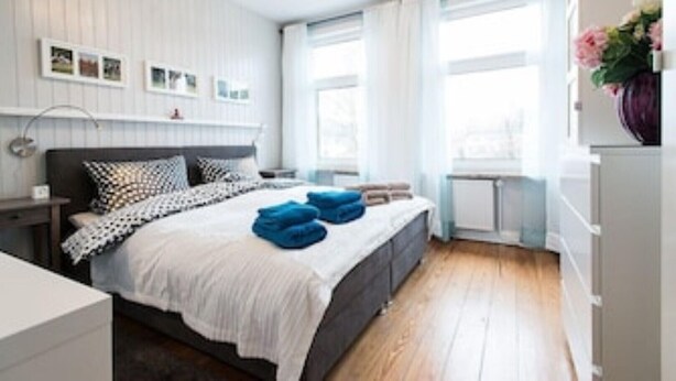 Une chambre à coucher moderne avec un lit, des tables de chevet et une fenêtre avec des rideaux.