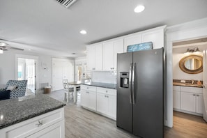 A modern kitchen with white cabinetry, a stainless steel refrigerator, and a granite countertop.