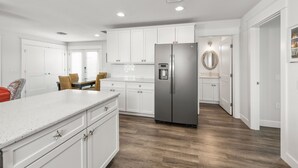 Una cocina moderna con armarios blancos, un refrigerador de acero inoxidable y una barra desayunadora.