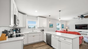 Una cocina moderna con armarios blancos, una isla central y un sofá rojo en la zona de estar contigua.
