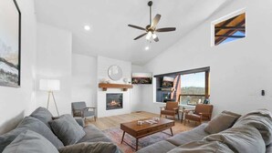 A modern living room with a fireplace, a ceiling fan, and a large window offering a view. - Lake View|Pools·Hot Tub·Sauna|Game&Theater Rm·18 (Indian Point)