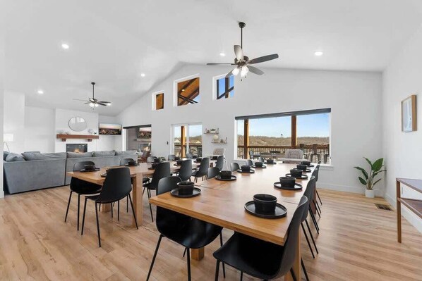 Une salle à manger spacieuse avec une longue table en bois, des chaises noires et un ventilateur de plafond.