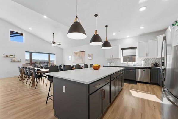 A modern kitchen with a large island, pendant lights, and stainless steel appliances.