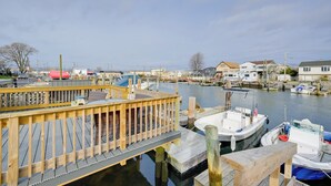 Een jachthaven met aangemeerde boten, een houten steiger en huizen op de achtergrond.