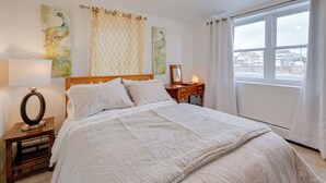Een netjes ingerichte slaapkamer met een groot bed, een nachtkastje met een lamp en een raam met gordijnen.