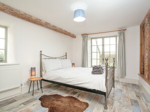 A bedroom with a metal bed frame, white bedding, a wooden floor, a fur rug, a bedside lamp, and a window with curtains. - 1 bedroom accommodation in Lympstone (Lympstone)