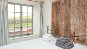A bedroom with a large window, a bed with white and grey linens, and a rustic wooden wall.