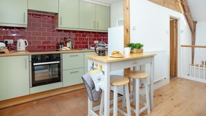 A kitchen with green cabinets, a red-tiled backsplash, a wooden beam ceiling, a white refrigerator, and a small bar area with stools.