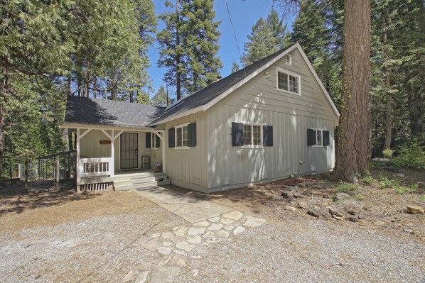 A single-story cabin with a stone-paved entrance, surrounded by tall trees. - The Cabin Viola (Shingletown)