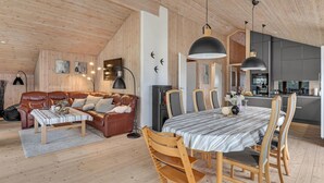 A cozy living room with a brown leather sofa, a dining table with striped tablecloth, and wooden chairs. - Stunning home in Aakirkeby with WiFi (Aakirkeby)