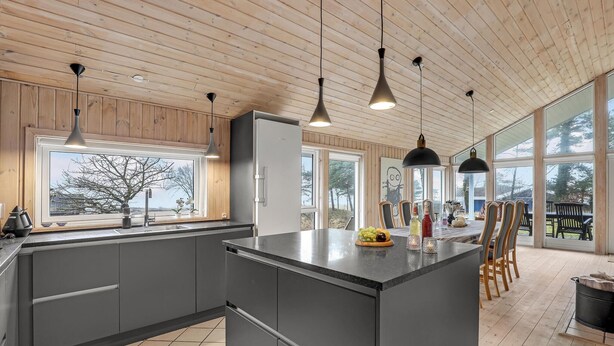 A modern kitchen with a large island, wooden ceiling, and large windows offering a view of the outdoors. - Stunning home in Aakirkeby with WiFi (Aakirkeby)
