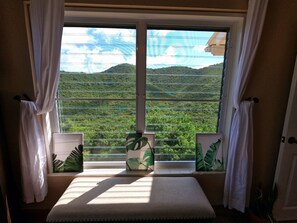 Enjoy a peaceful retreat with a serene view of the lush landscape from the large window, complemented by botanical prints and a cozy bench.