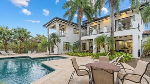 A modern two-story house with a pool, outdoor seating, and palm trees.